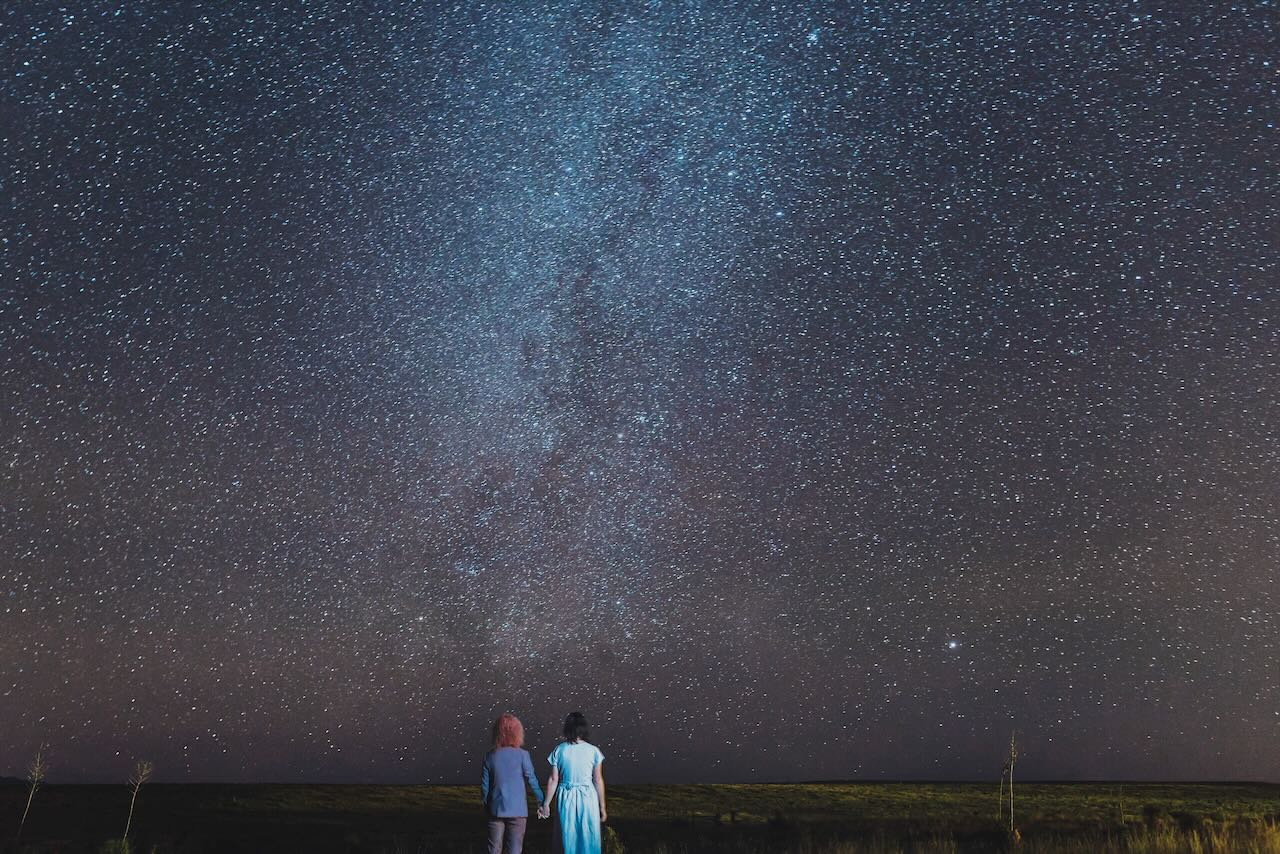 Carol and Dorian standing together under the stars in West Texas. The Milky Way is prominent in the center of the photo.